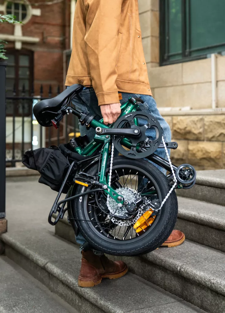 Engwe Zip lightweight folding electric bike folded up in the colour green and being carried up stairs