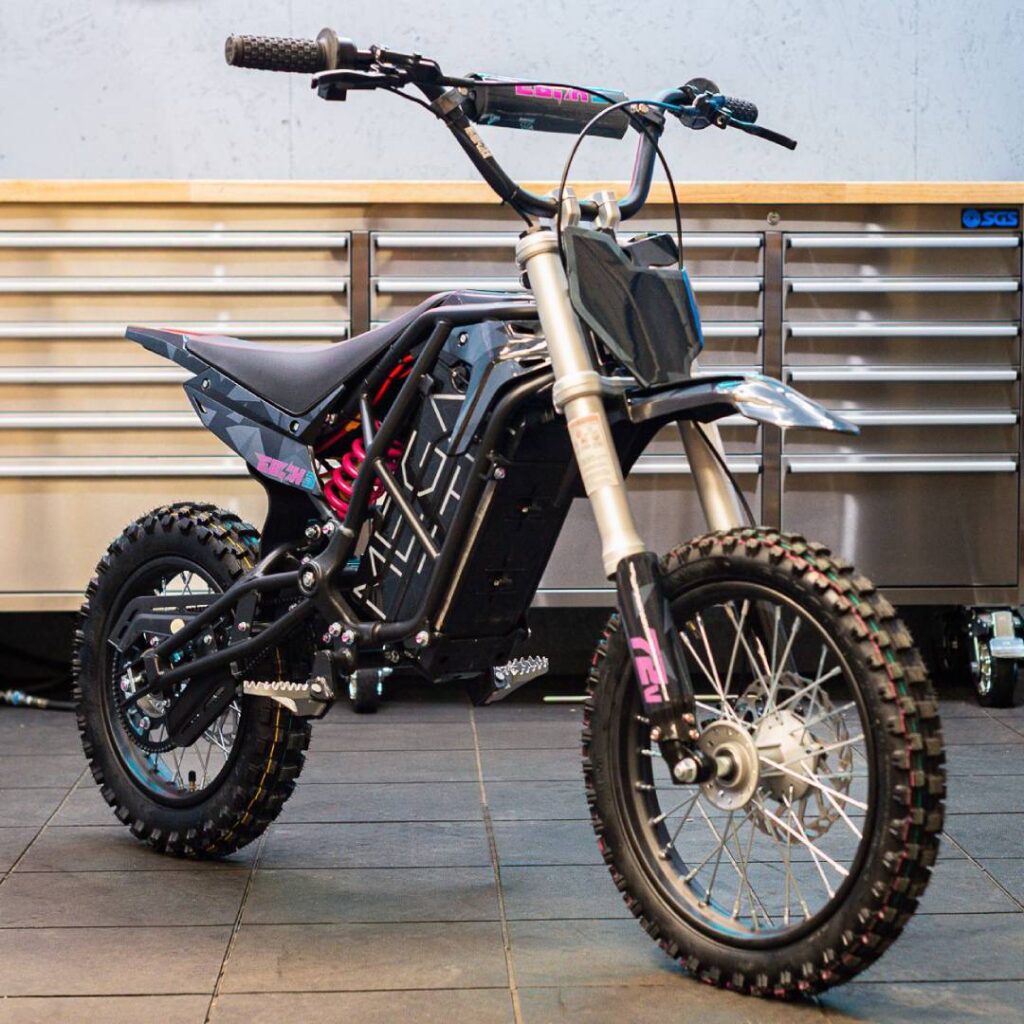 EBOX 3 MX Electric Minibike in orange, full side view on workshop floor, highlighting double-cradle steel frame, suspension, and compact off-road build.